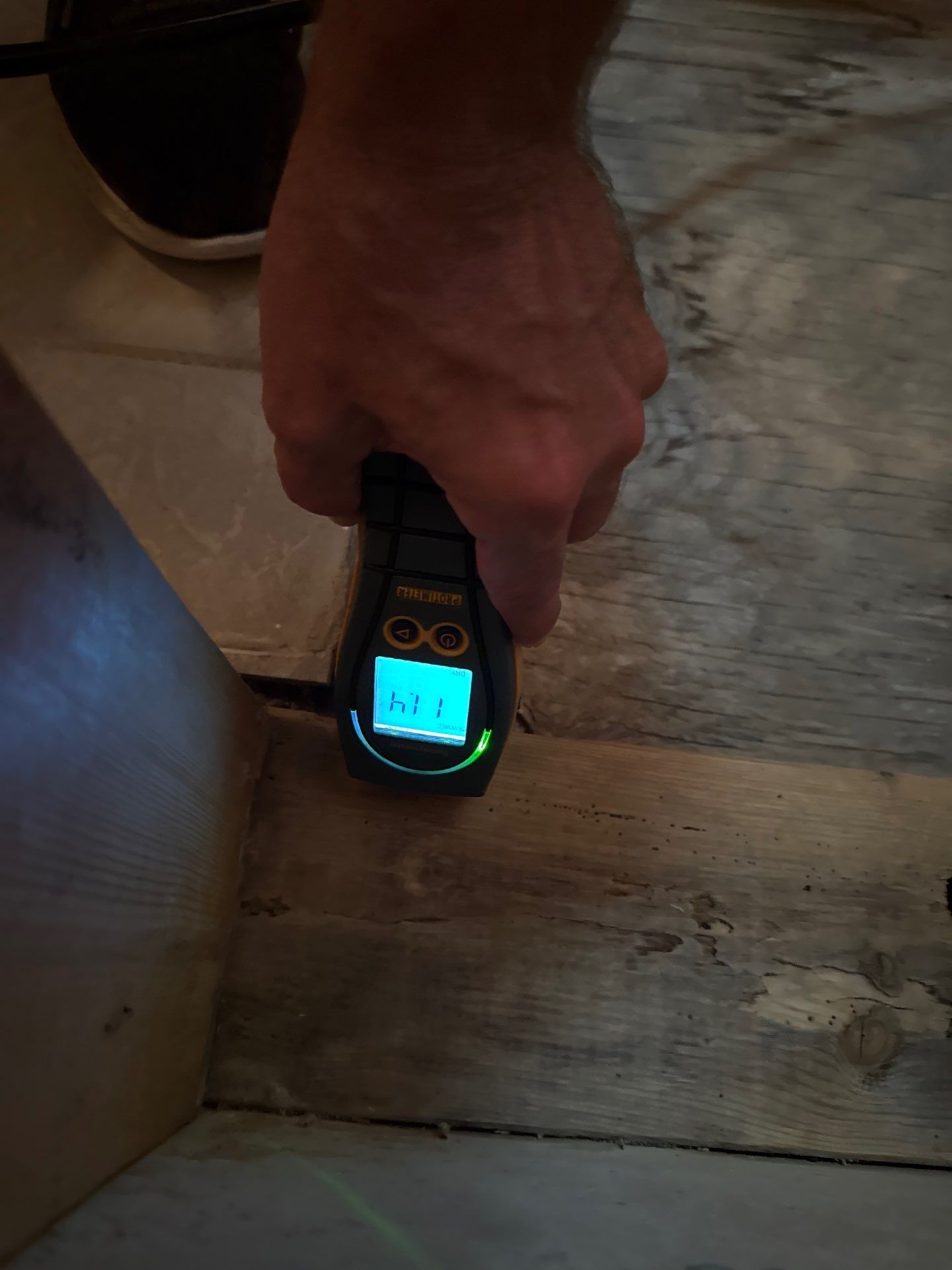 Close-up of a technician using a moisture probe to test the moisture content of subfloor wood during remediation.