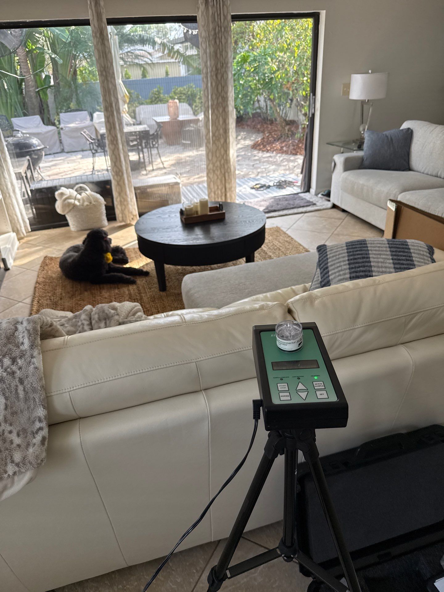 Final air quality sampling pump set up on a tripod in a living room for post-remediation clearance testing.