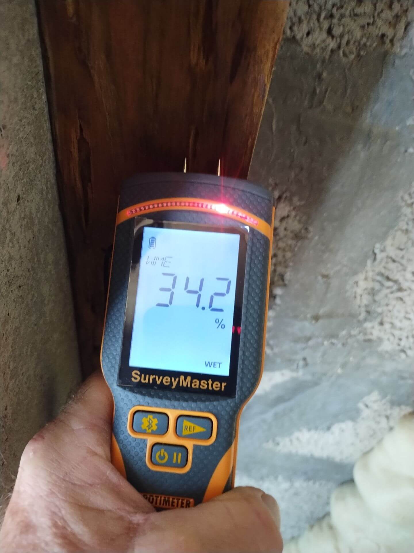 Using a Protimeter SurveyMaster pin meter to measure high moisture content in a structural wood beam during a water damage assessment.
