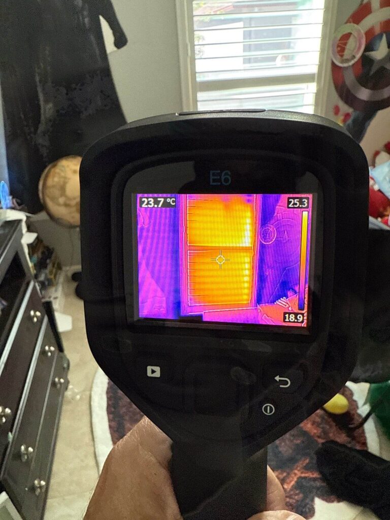 FLIR thermal imaging camera display showing heat loss and potential air leaks around a residential window.