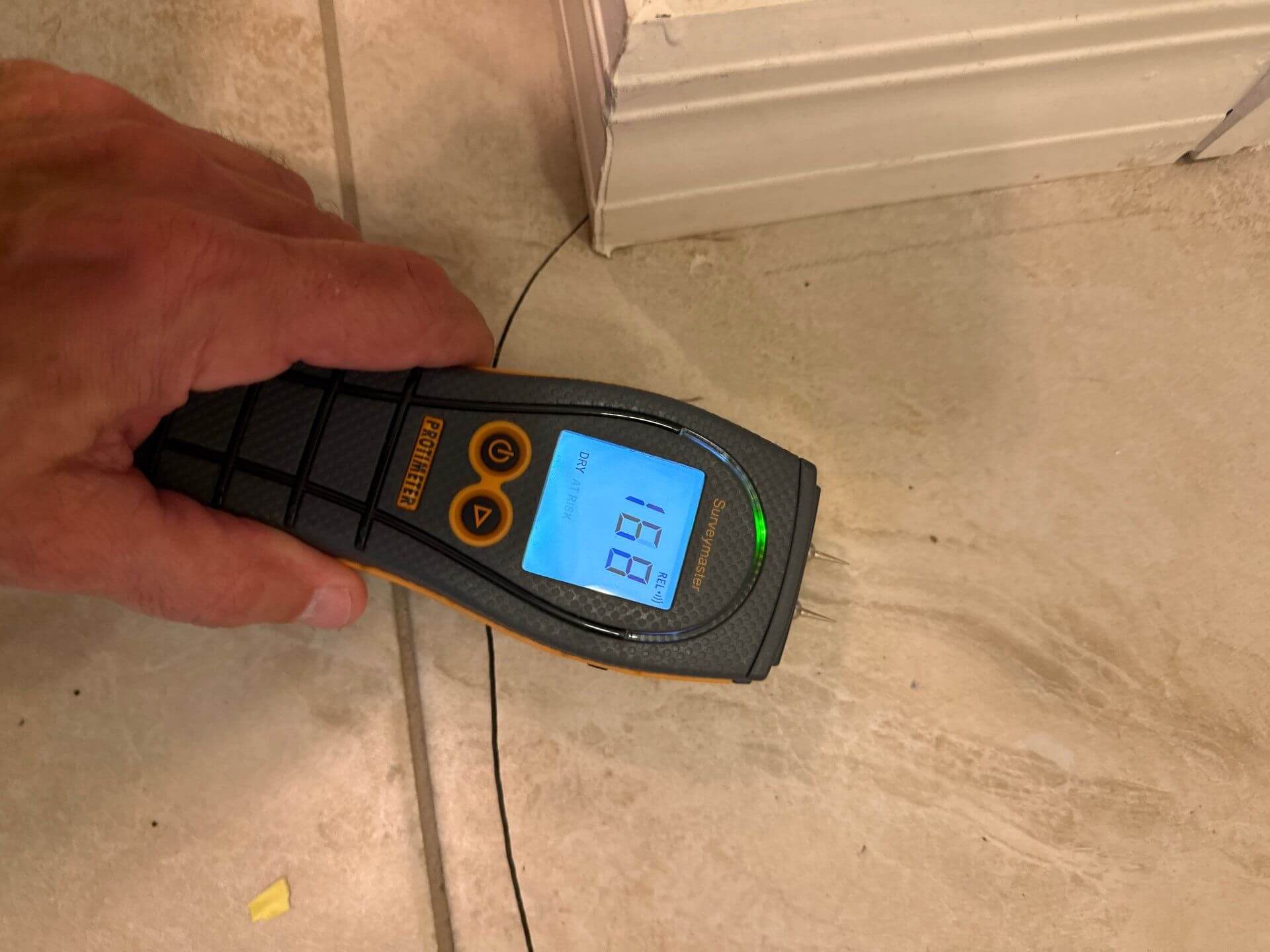 Protimeter Surveymaster measuring moisture levels in a ceramic tile floor to detect subfloor water damage.