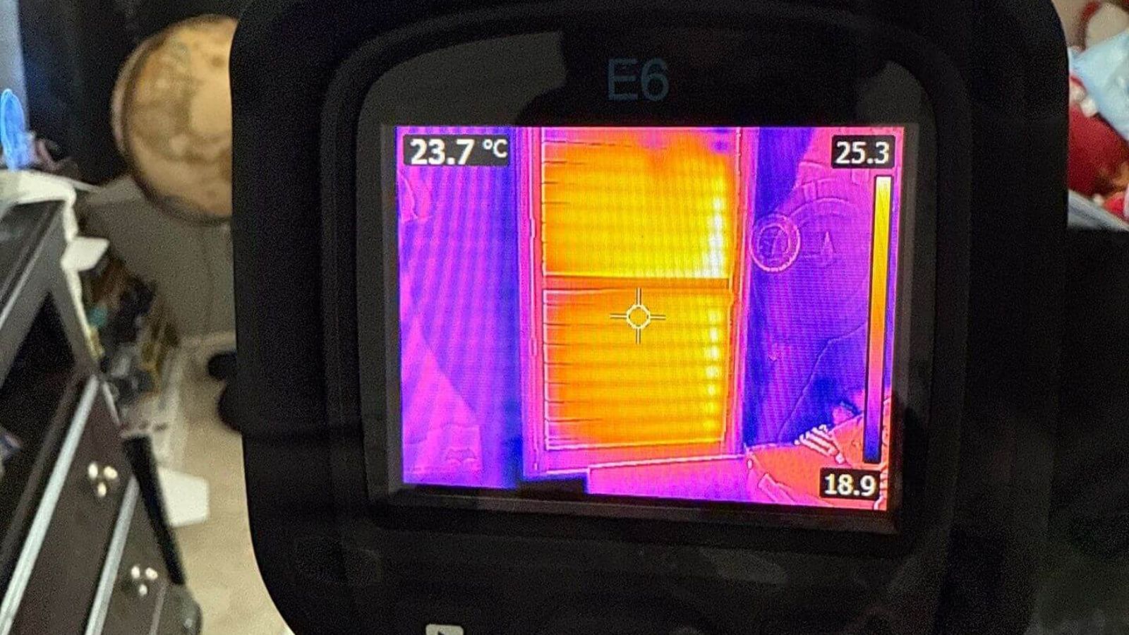 Thermal imaging camera detecting heat differences on a window and wall inside a home.