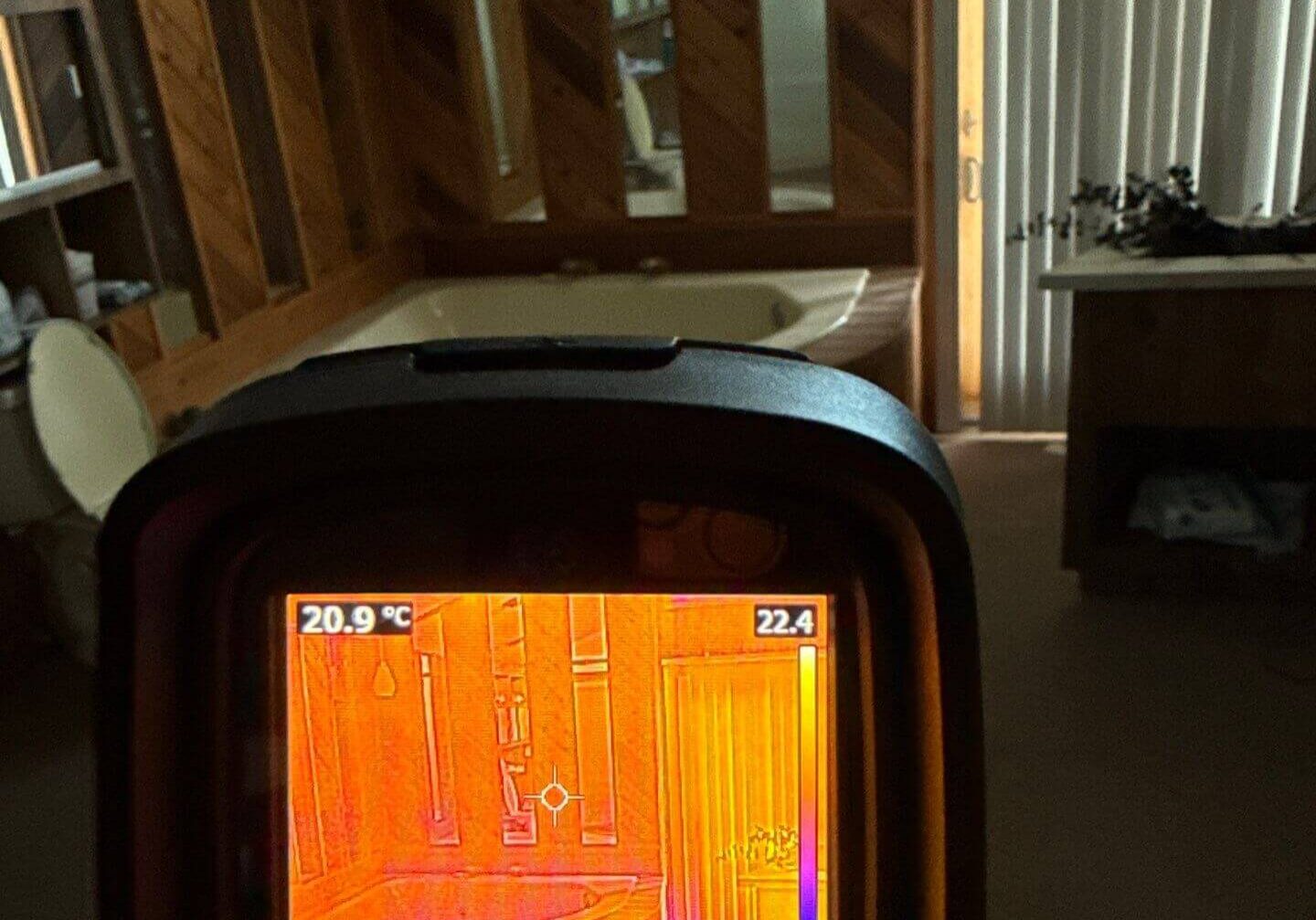 Infrared thermal camera screen identifying temperature anomalies around a bathroom garden tub and wood paneling.