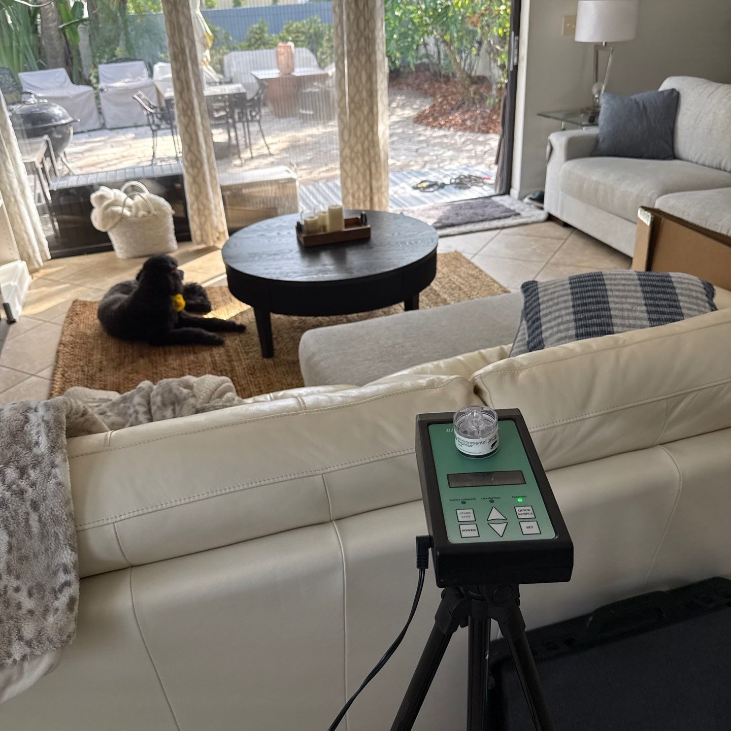 Final air quality sampling pump set up on a tripod in a living room for post-remediation clearance testing.