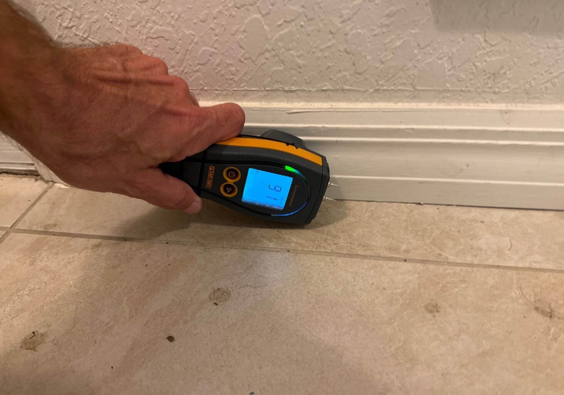 Close-up of a moisture meter checking for water intrusion behind baseboards during a leak investigation.