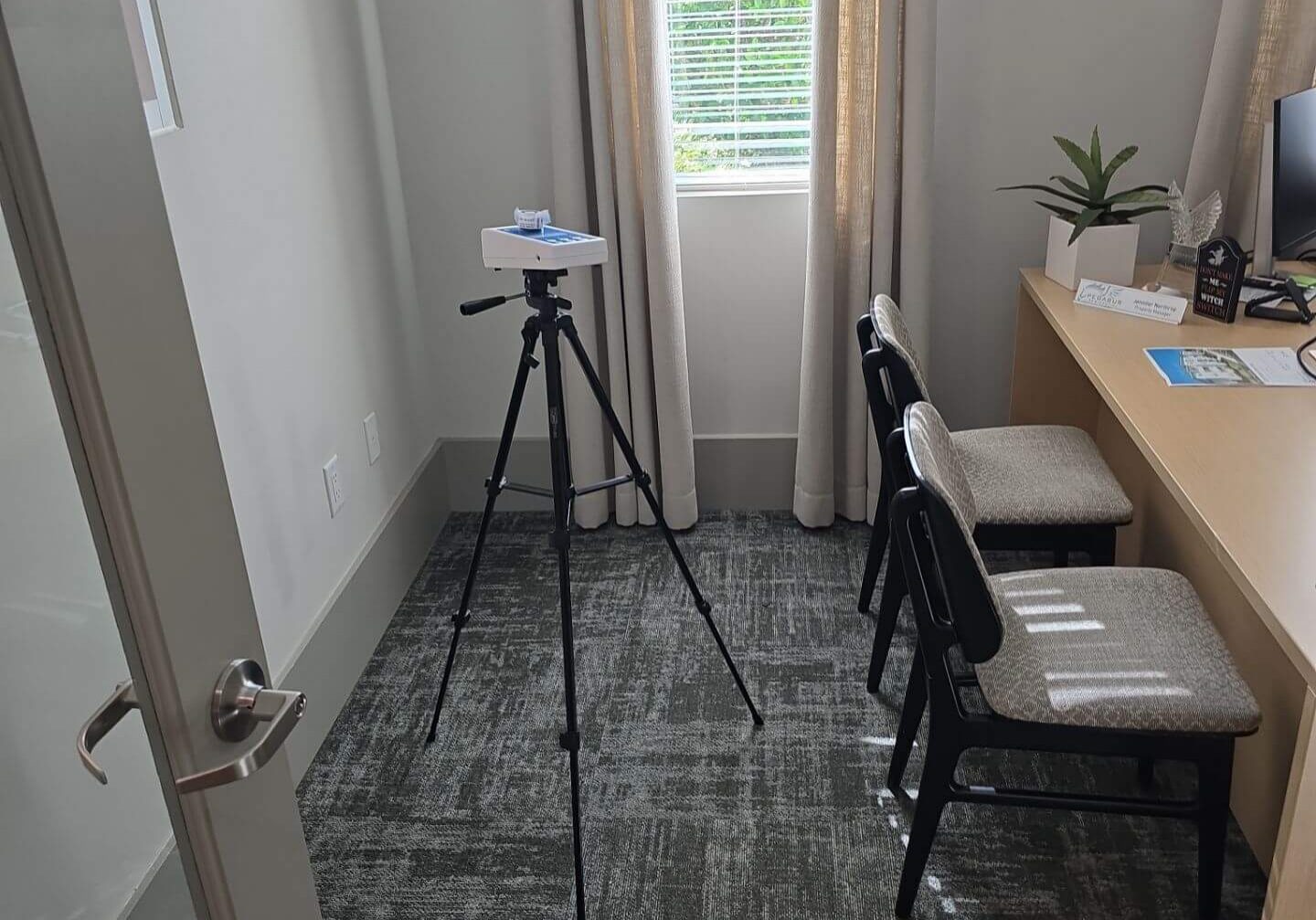 Portable air quality sensor mounted on a tripod performing an environmental health assessment in a private office space.