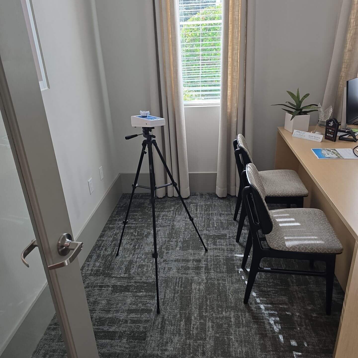 Portable air quality sensor mounted on a tripod performing an environmental health assessment in a private office space.