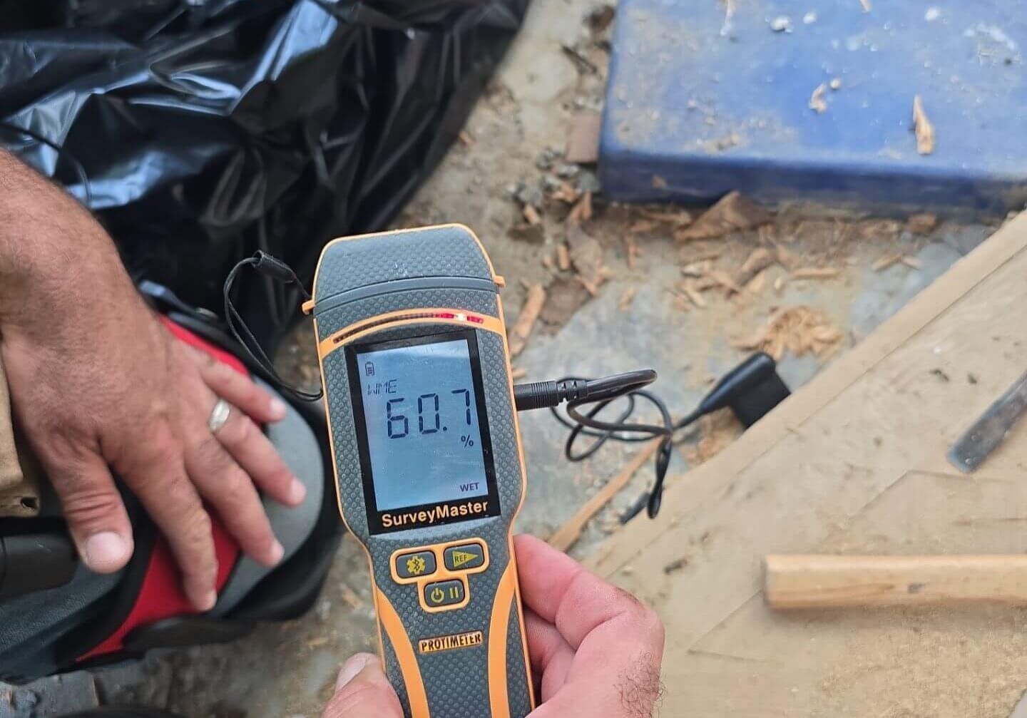 Professional moisture meter testing the Wood Moisture Equivalent (WME) of a subfloor to determine the extent of water saturation.