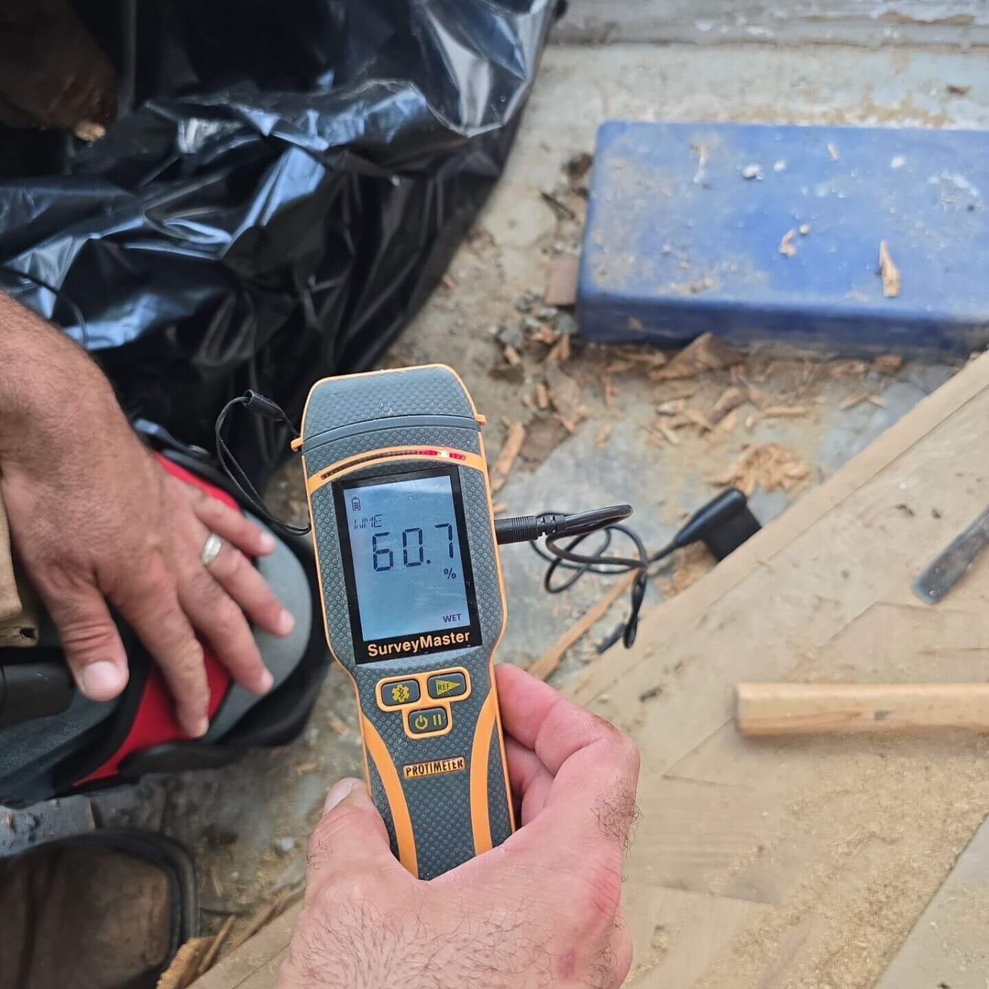 Professional moisture meter testing the Wood Moisture Equivalent (WME) of a subfloor to determine the extent of water saturation.