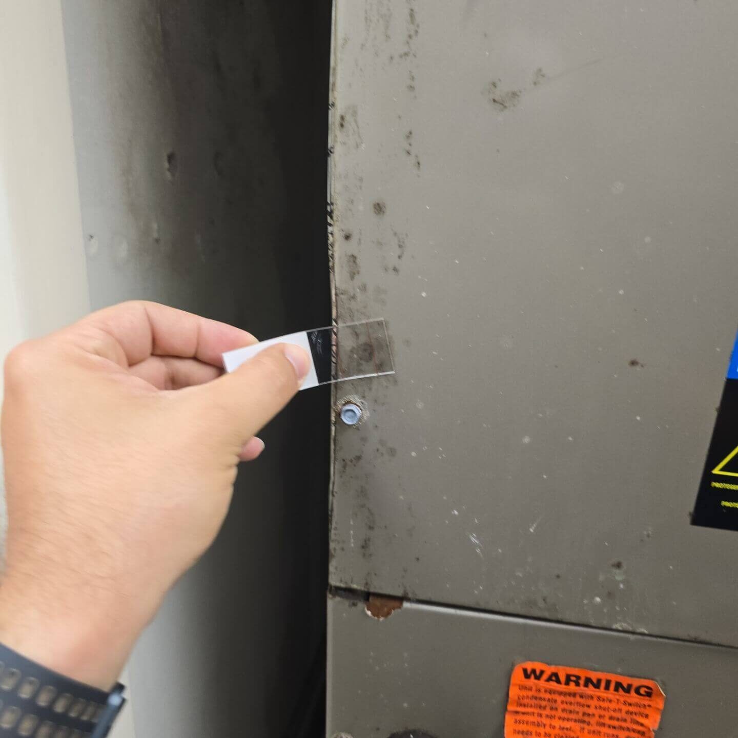 An environmental technician performing a bio-tape lift sample on an HVAC unit for laboratory mold analysis.