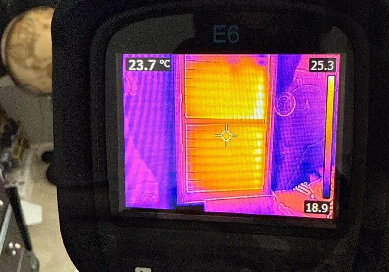 Thermal imaging camera detecting heat differences on a window and wall inside a home.