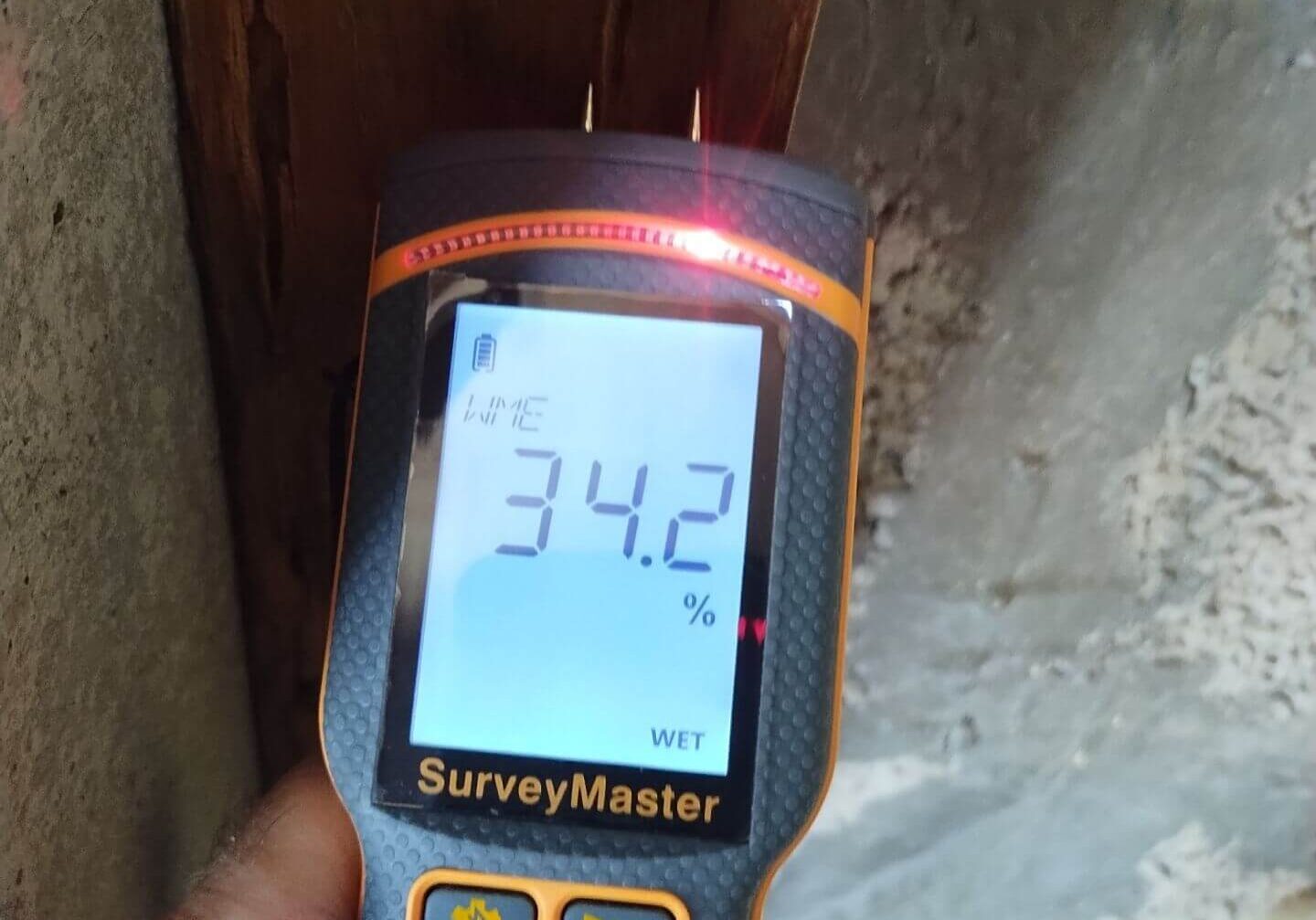 Using a Protimeter SurveyMaster pin meter to measure high moisture content in a structural wood beam during a water damage assessment.