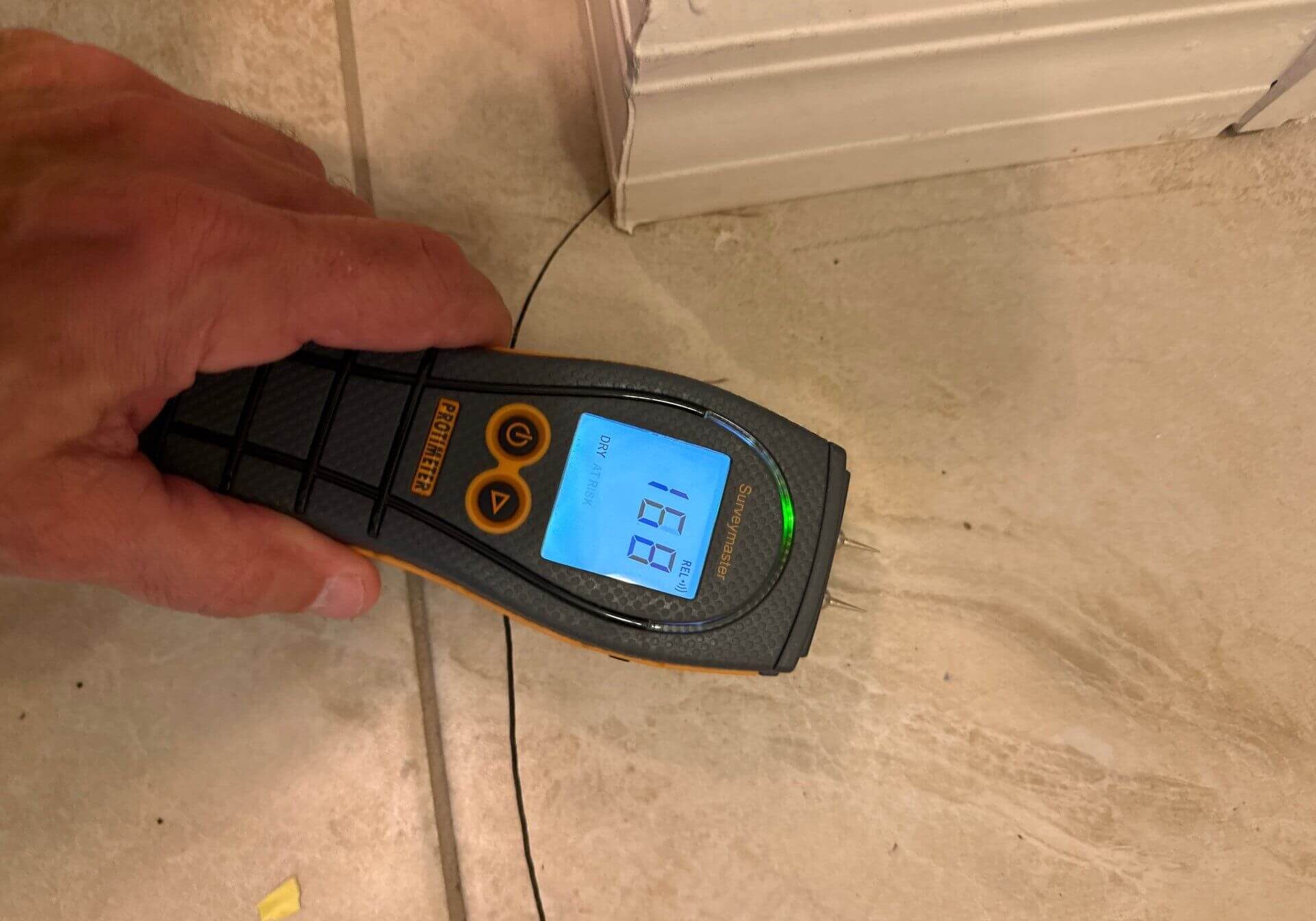 Protimeter Surveymaster measuring moisture levels in a ceramic tile floor to detect subfloor water damage.